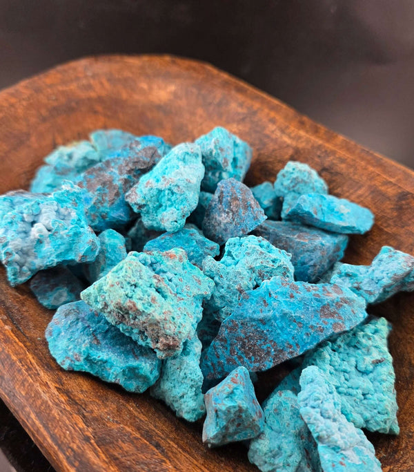 Raw chrysocolla stones showcasing vibrant blue and green hues, displayed in a wooden bowl.
