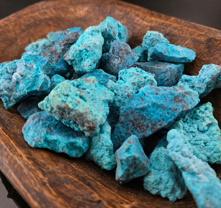 Raw chrysocolla stones in vibrant blue and green hues displayed on a wooden dish.