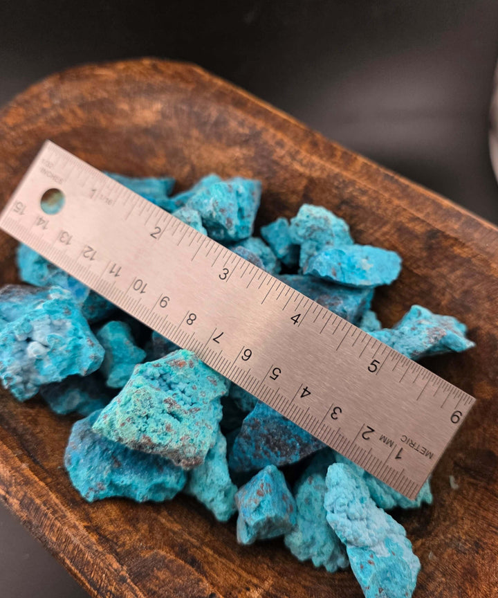 Raw chrysocolla stones displaying vibrant blues and greens, with a ruler for size comparison.