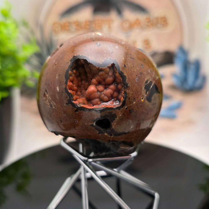 Red Fox Agate Sphere displayed in a stand, showcasing its shiny surface and unique cavities.