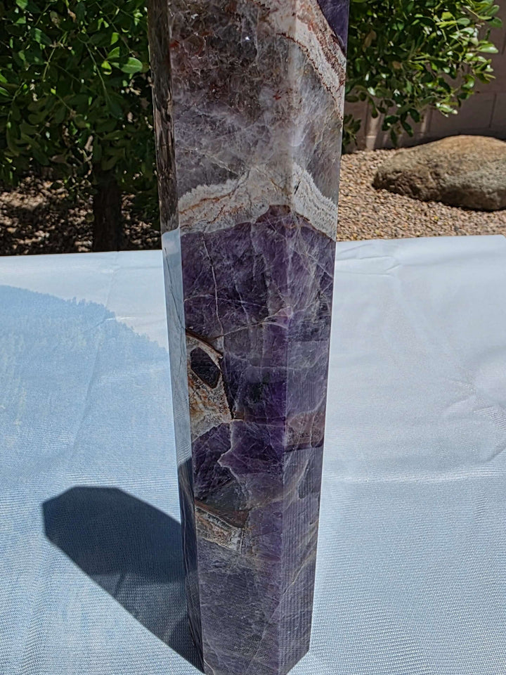 Beautiful chevron amethyst tower with deep purple colors, excellent point, and steady base. Picture taken on sunlight to show the beautiful colors. Over a foot tall with beaitiful polish Chevron amethyst, also known as banded amethyst or dream amethyst, i