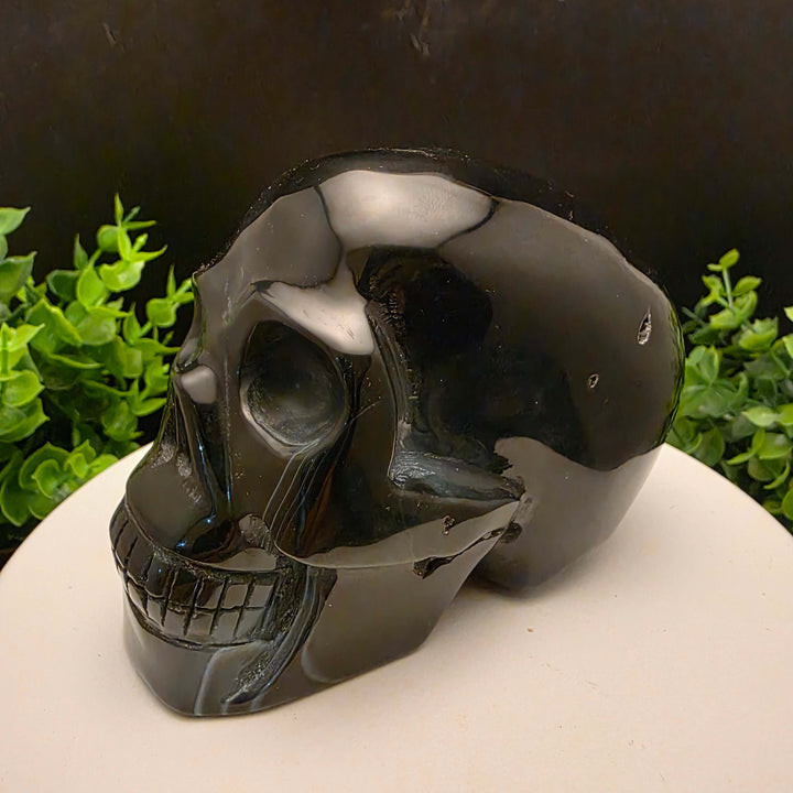 Black Banded Agate Skull Carving - 4 Inch displayed on a stand, showcasing dark stone and blue bands.