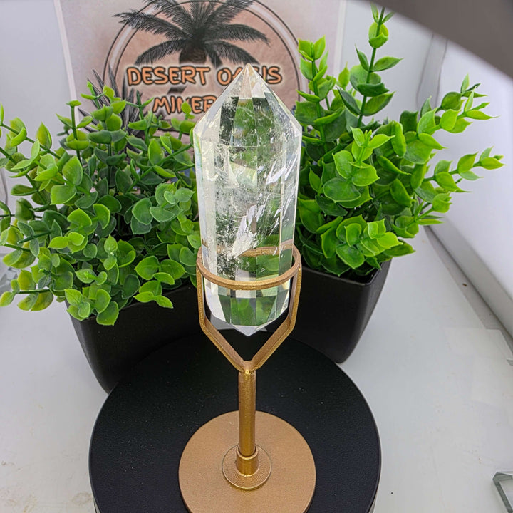Polished Faceted Clear Quartz Crystal with Stand displayed among greenery.
