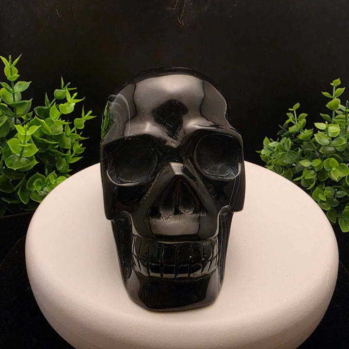 Black Banded Agate Skull Carving - 4 Inch displayed on a stand, showcasing dark stone and blue bands.