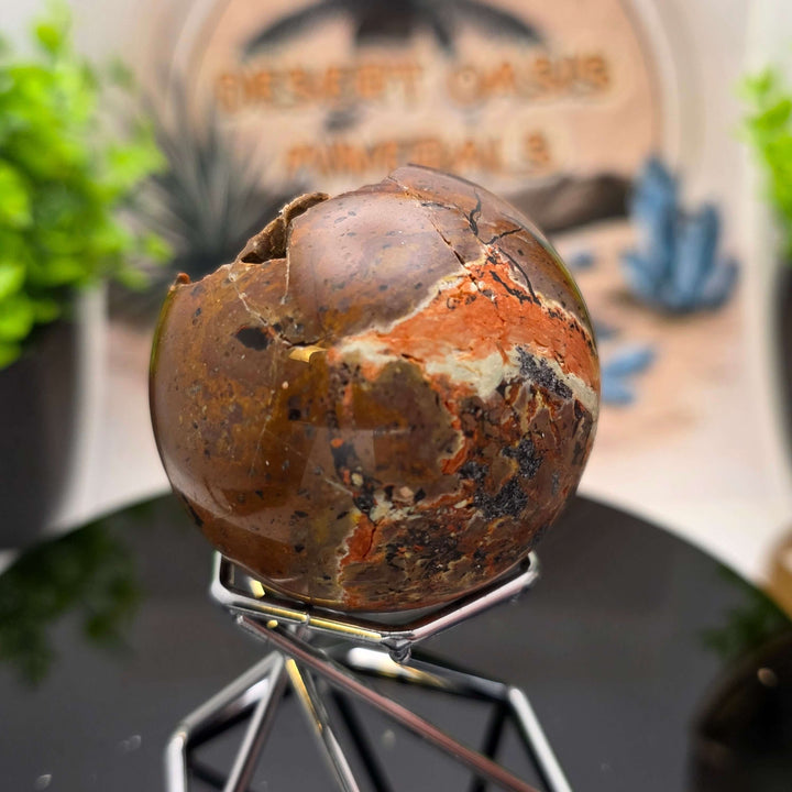 Red Fox Agate Sphere displayed in a stand, showcasing its shiny surface and unique cavities.