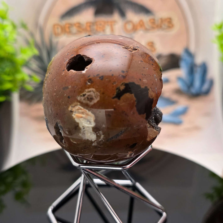 Red Fox Agate Sphere displayed in a stand, showcasing its shiny surface and unique cavities.