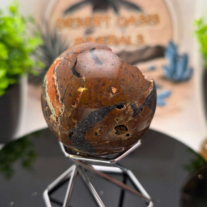 Red Fox Agate Sphere displayed in a stand, showcasing its shiny surface and unique cavities.
