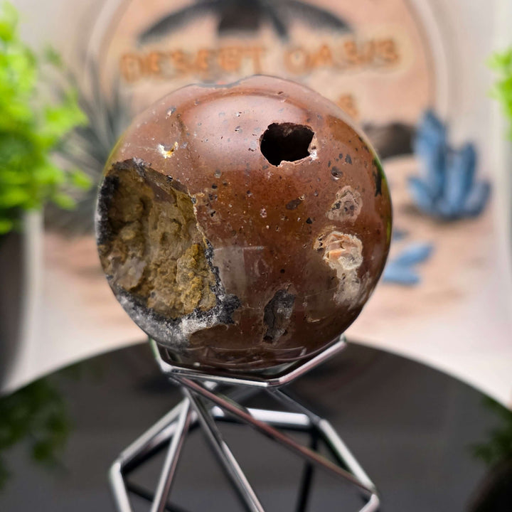 Red Fox Agate Sphere displayed in a stand, showcasing its shiny surface and unique cavities.