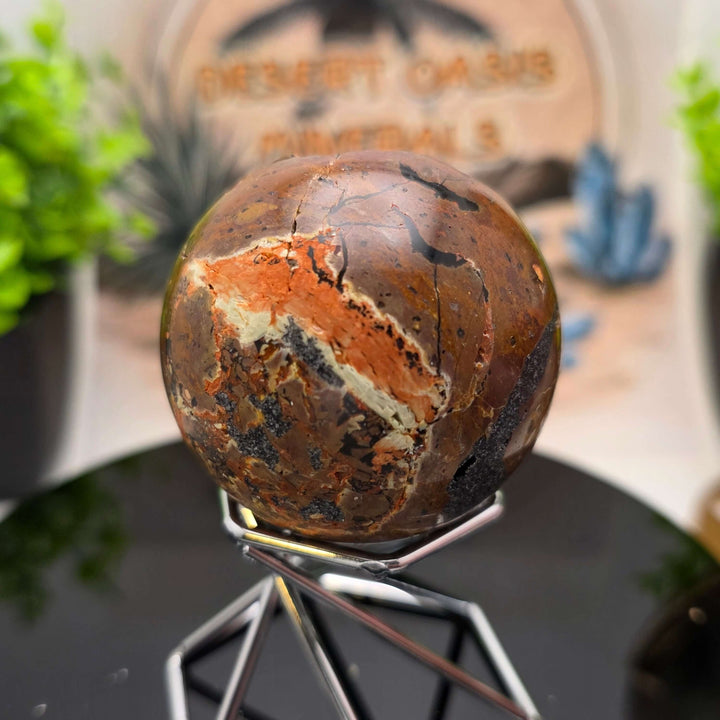 Red Fox Agate Sphere displayed in a stand, showcasing its shiny surface and unique cavities.