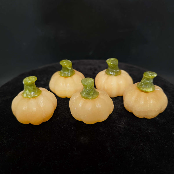 Five small orange calcite pumpkin carvings with green stems on a black surface.