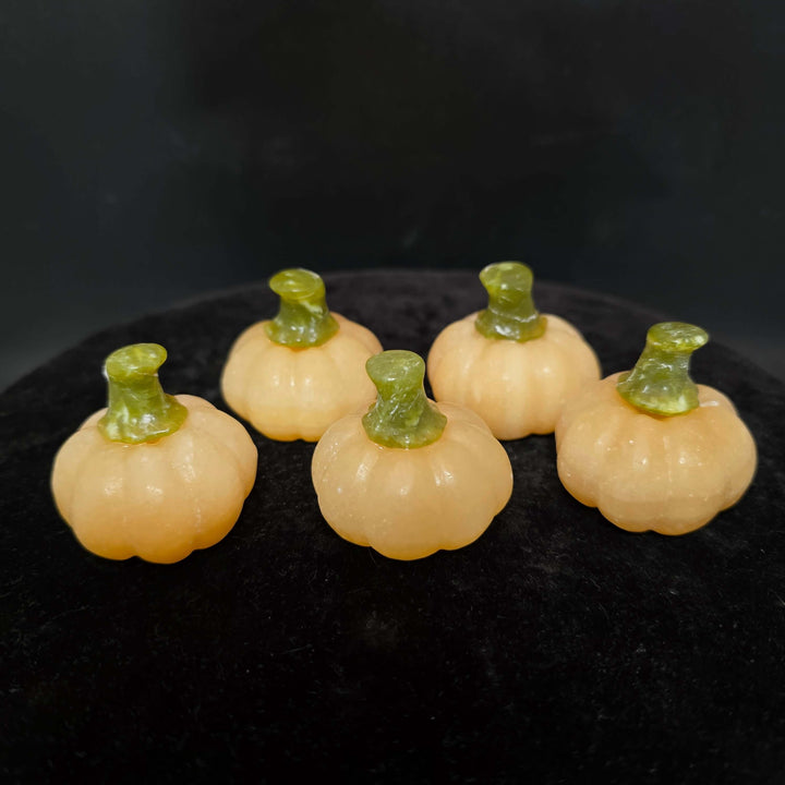 Five small orange calcite pumpkin carvings with green stems on a black surface.