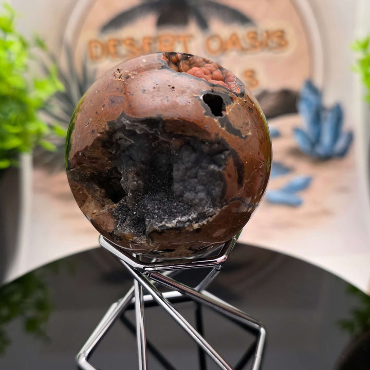 Red Fox Agate Sphere displayed in a stand, showcasing its shiny surface and unique cavities.