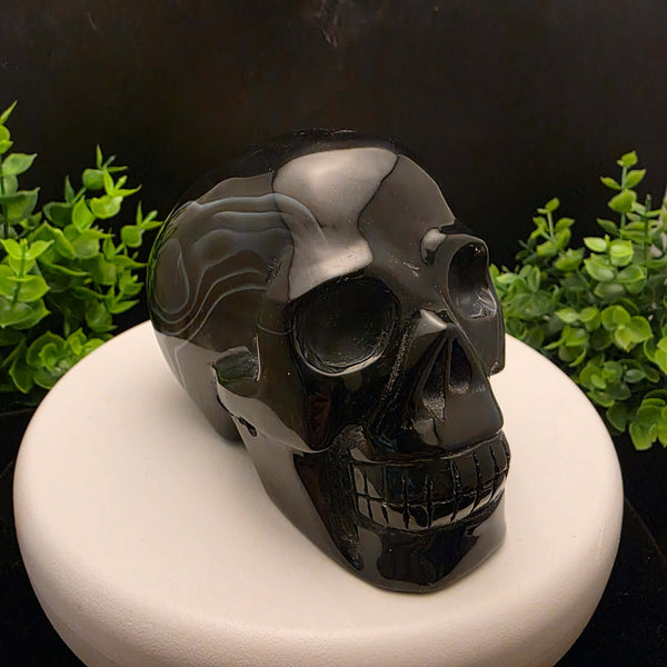 Black Banded Agate Skull Carving - 4 Inch displayed on a stand, showcasing dark stone and blue bands.