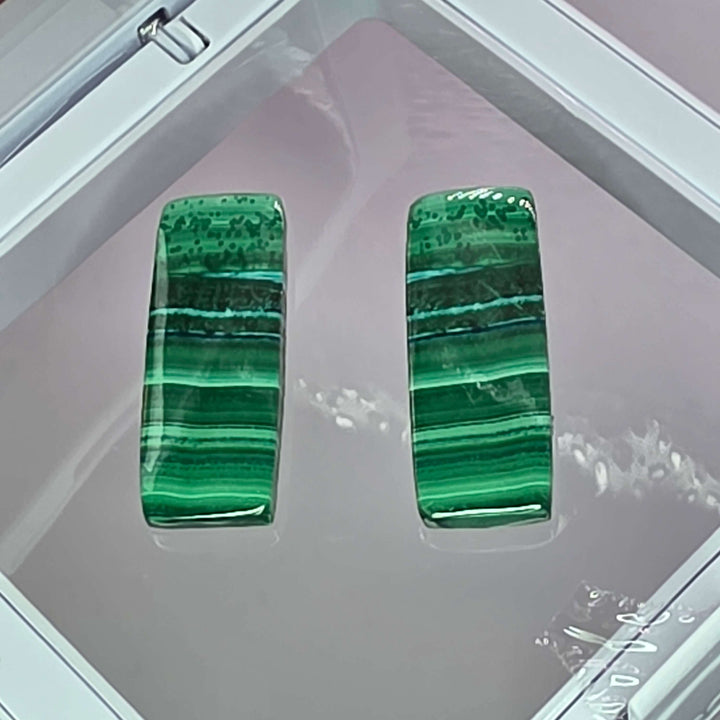 Bring the vibrant energy of nature into your home, or your next creative project, with our stunning Malachite Cabochon Pairs. Each pair features beautifully polished malachite, showcasing its unique swirling patterns, elegantly presented in a crisp white