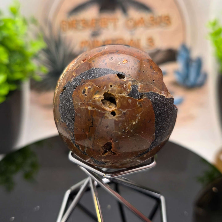 Red Fox Agate Sphere displayed in a stand, showcasing its shiny surface and unique cavities.