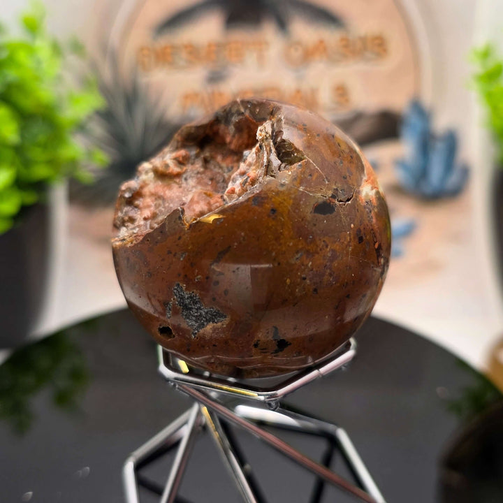 Red Fox Agate Sphere displayed in a stand, showcasing its shiny surface and unique cavities.
