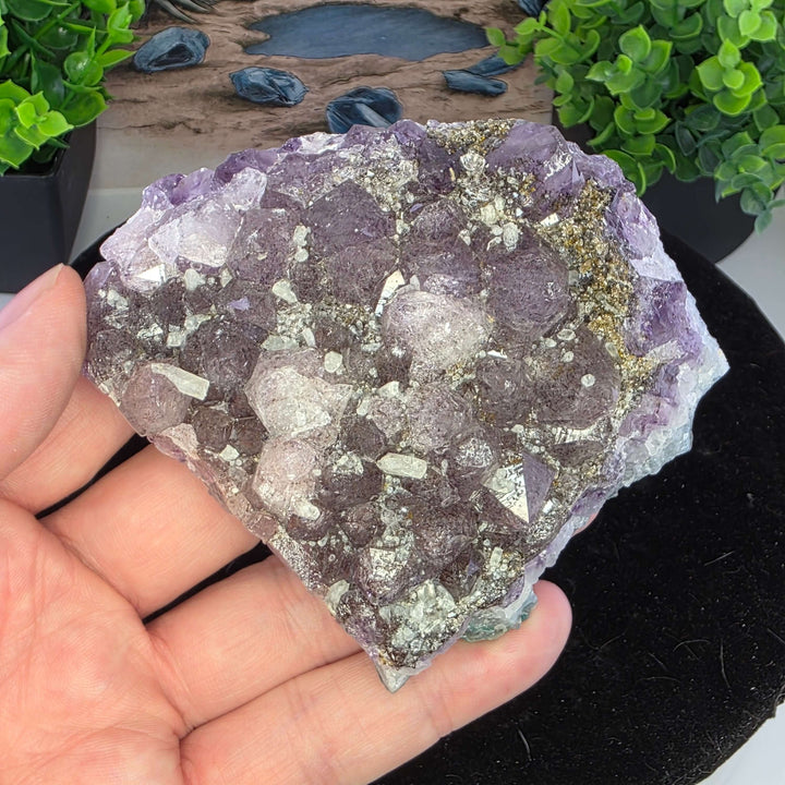 Embrace the raw beauty of nature with this unique Amethyst Geode Cluster. While it carries minor natural inclusions—perhaps hints of earthy hematite or other intriguing minerals—and some gentle signs of its journey, these features only add to its authenti