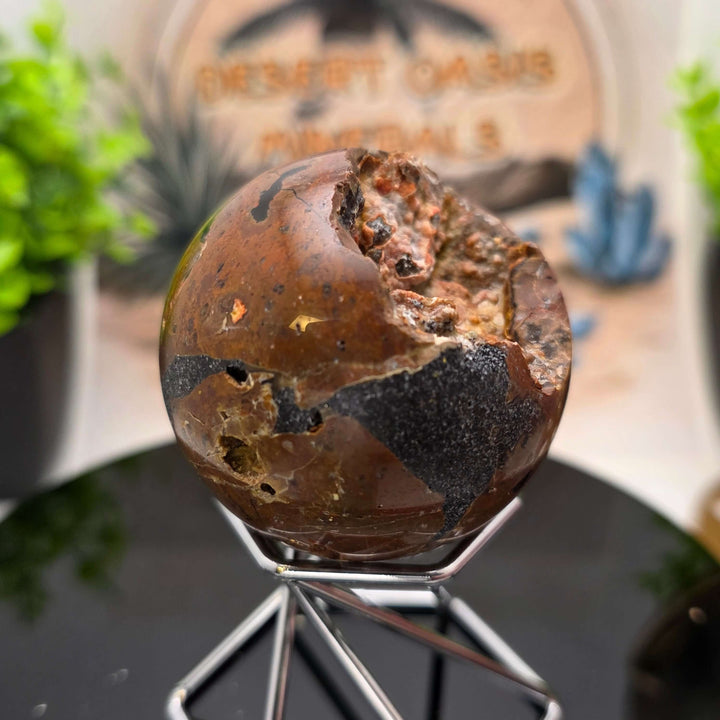 Red Fox Agate Sphere displayed in a stand, showcasing its shiny surface and unique cavities.